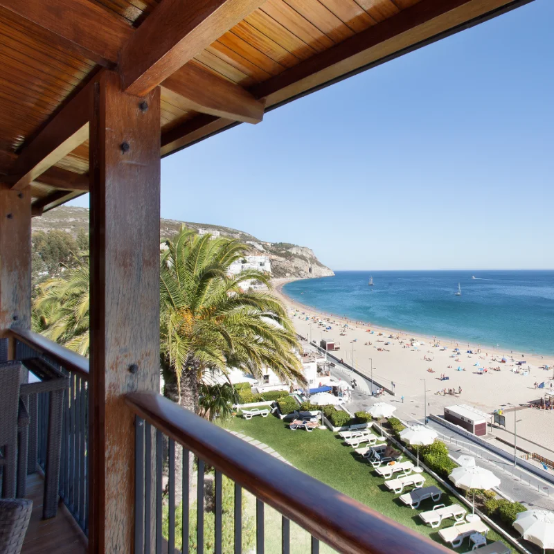 Varanda com vista para praia ensolarada e mar azul.