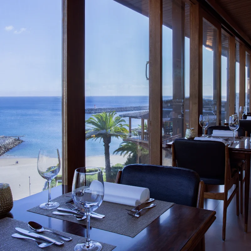 Restaurante &agrave; beira-mar com mesas vistas para o oceano e palmeiras.