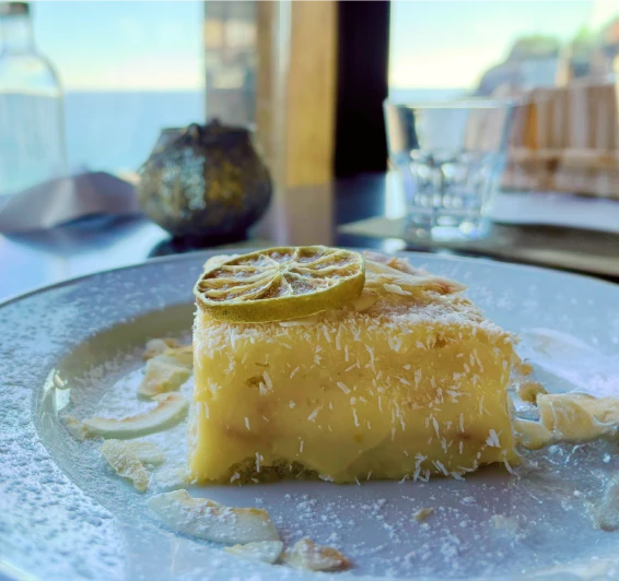 Sobremesa coberta com coco ralado e fatia de lim&atilde;o em prato branco.