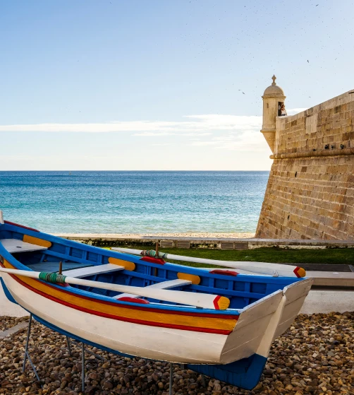 Barco colorido em frente ao mar, ao lado de uma muralha.