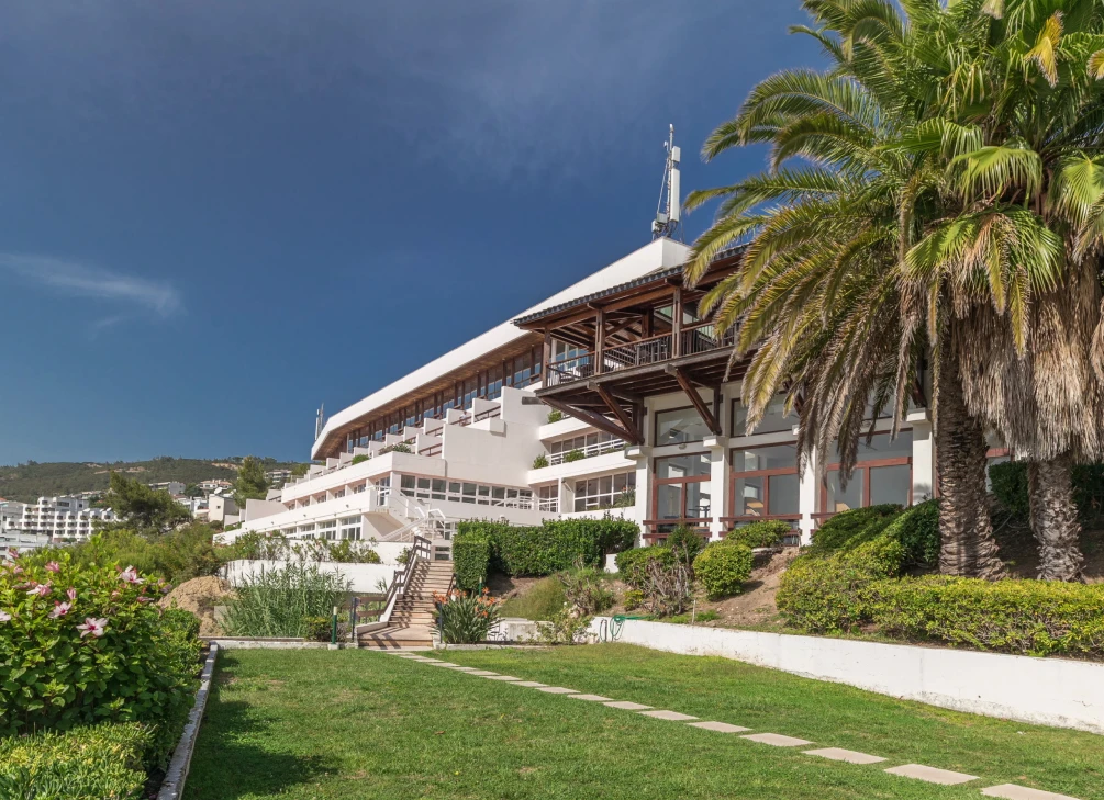 Edif&iacute;cio moderno rodeado por palmeiras e vegeta&ccedil;&atilde;o.
