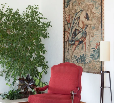 Cadeira vermelha e planta ao lado de tape&ccedil;aria em uma sala iluminada.