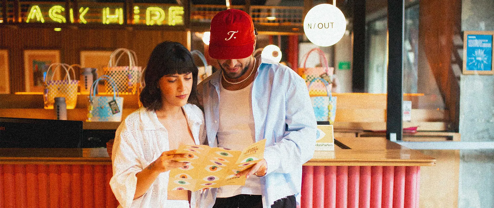 Dos personas leyendo un men&uacute; en un mostrador, con bolsas coloridas detr&aacute;s.