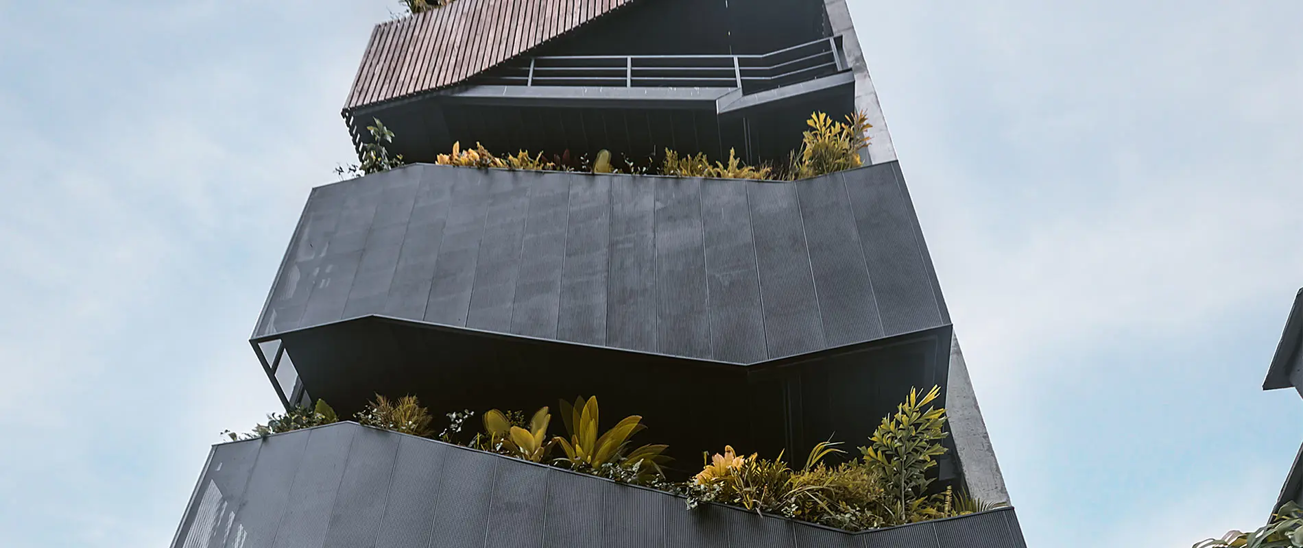 Edificio angular gris con vegetaci&oacute;n en sus balcones.