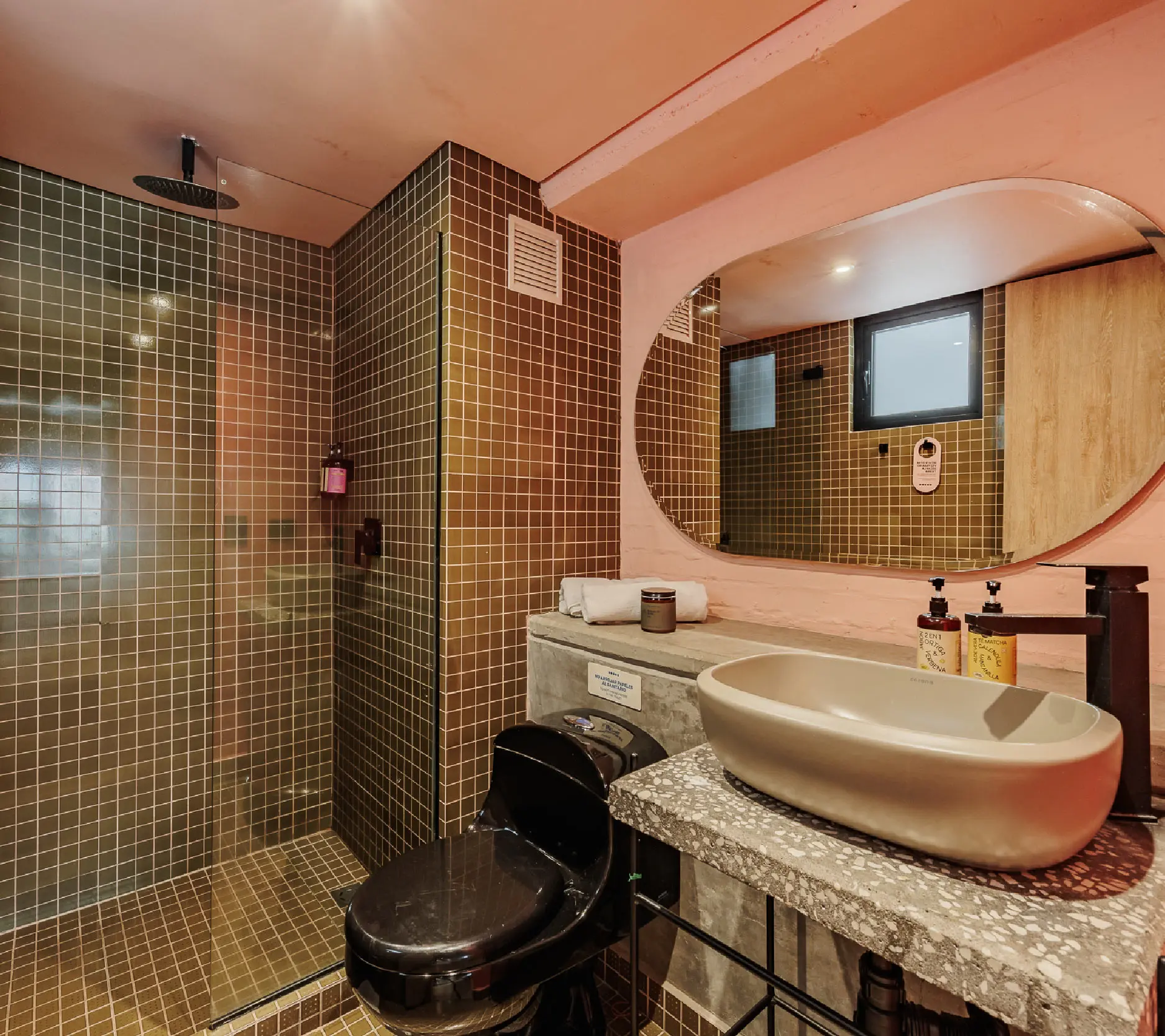 Ba&ntilde;o moderno con azulejos marrones, lavabo ovalado y espejo grande.