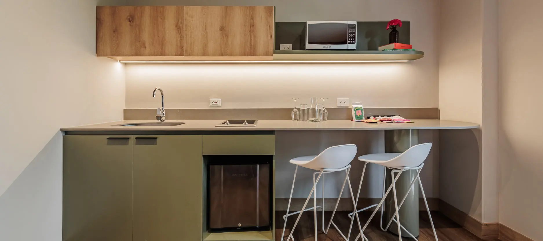 Cocina peque&ntilde;a moderna con barra, dos sillas y encimeras claras.