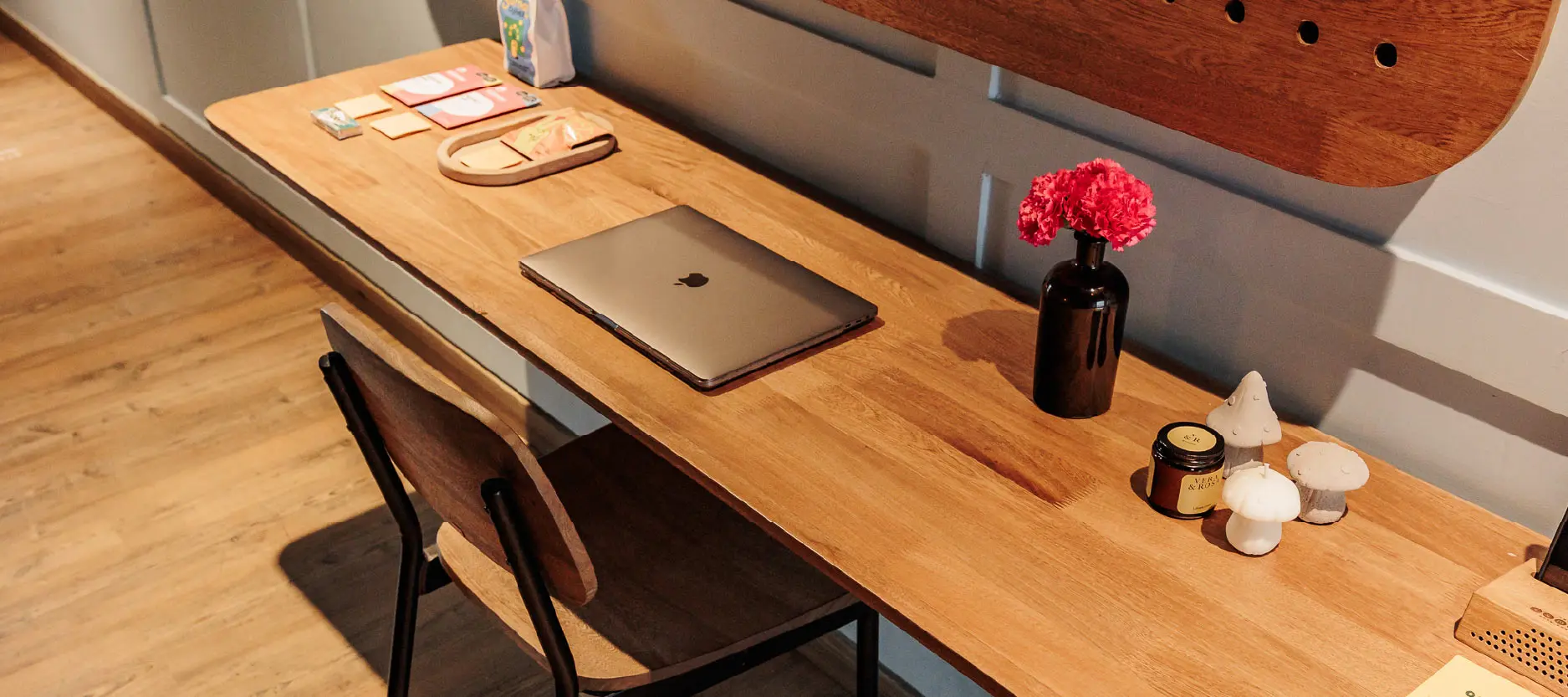 Escritorio con laptop, flores rojas en jarr&oacute;n negro y velas decorativas de hongos.