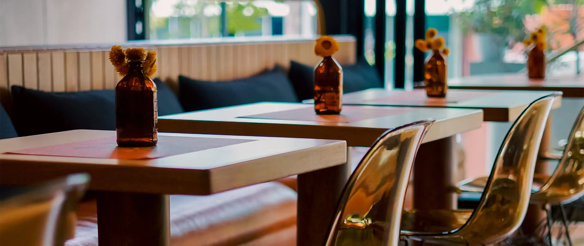 Mesas de caf&eacute; con botellas y flores, sillas transparentes alrededor.