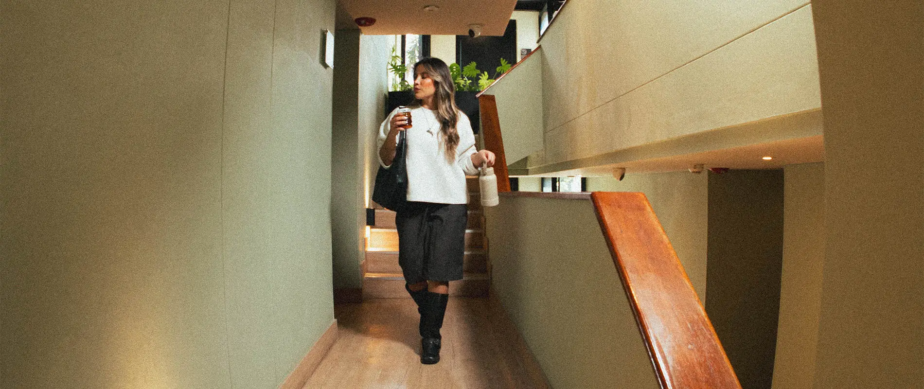 Mujer caminando en un pasillo con bebida y bolso.