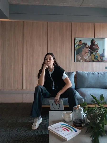 Mujer sentada en sof&aacute; moderno con cuadro al fondo y mesa con libro y caf&eacute;.