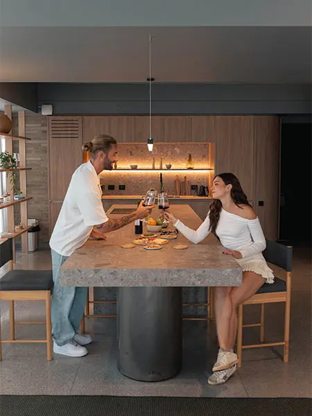 Una pareja brinda en la cocina moderna junto a una mesa r&uacute;stica.