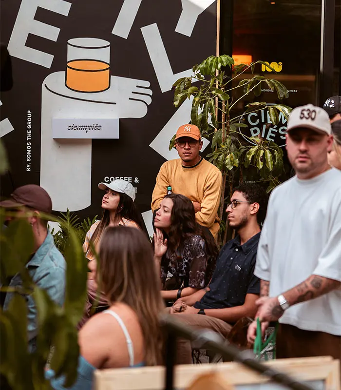 Personas sentadas en un evento con un cartel de bebida al fondo.