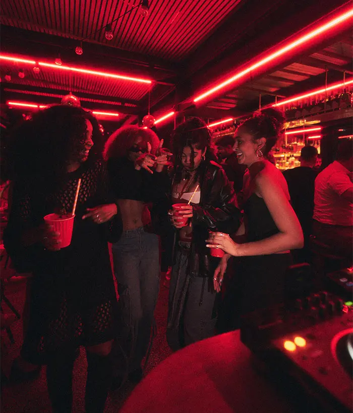 Personas bailando y riendo en una fiesta con luces rojas.