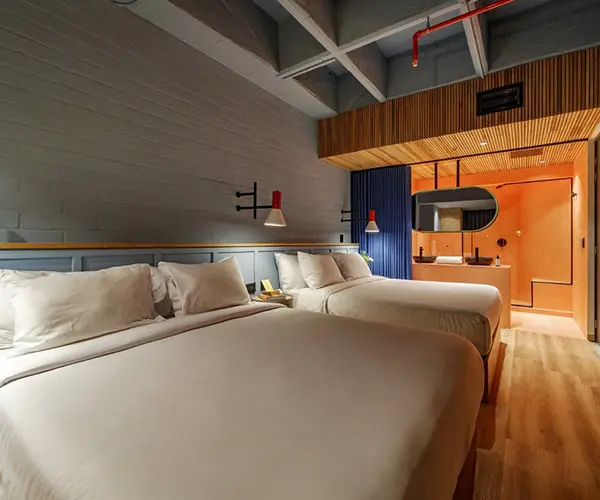 Habitaci&oacute;n de hotel moderna con dos camas y l&aacute;mparas de pared.