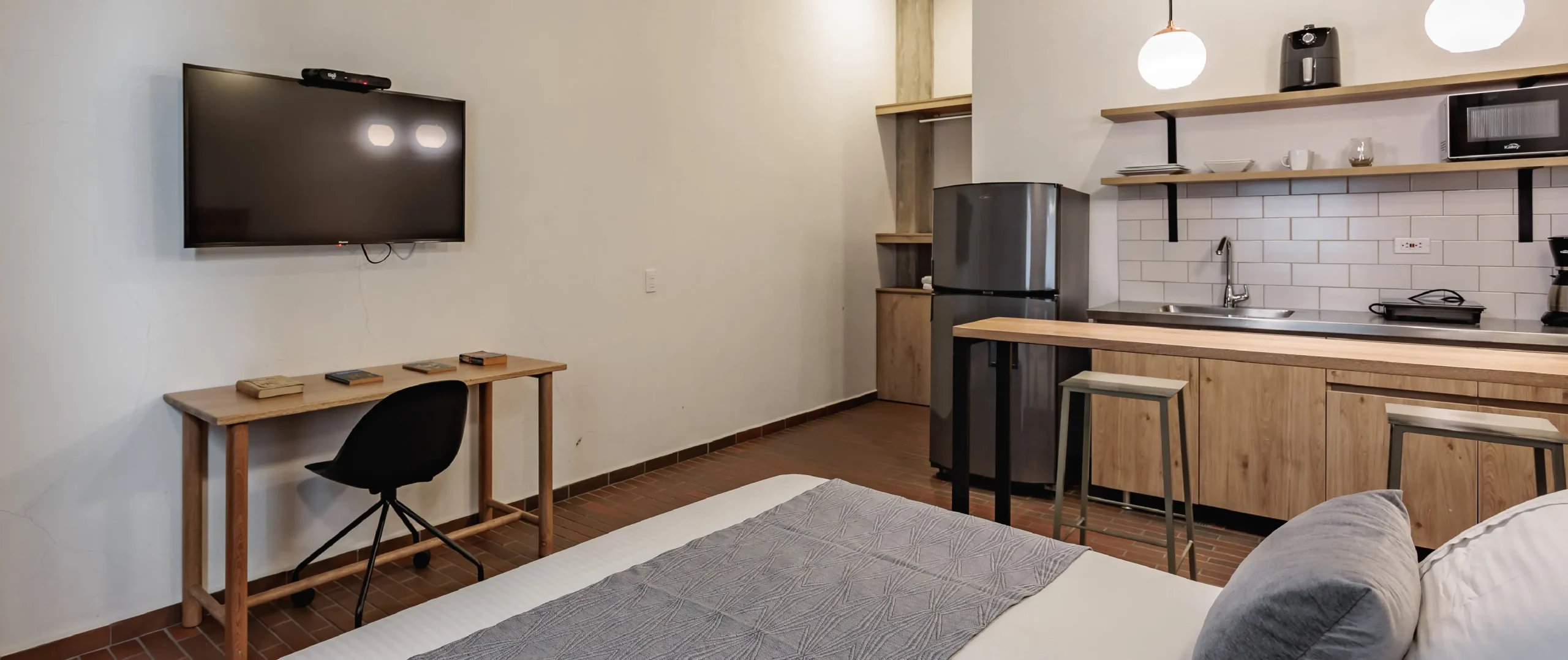Sala con cocina integrada, escritorio y televisor montado en la pared.