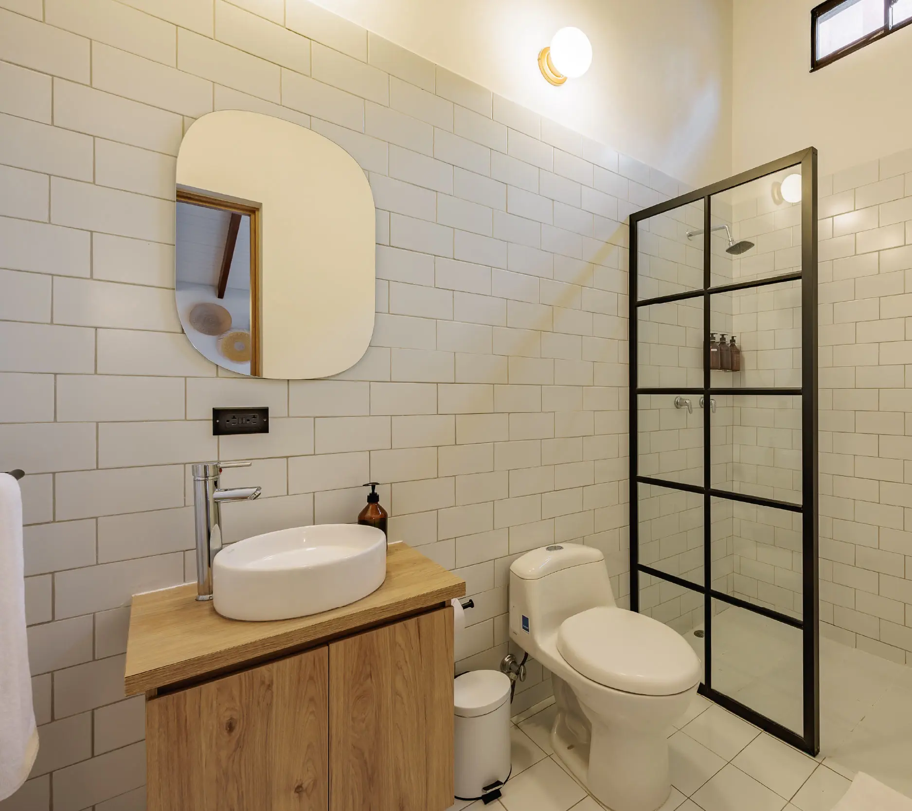 Ba&ntilde;o moderno con ducha de vidrio, lavabo y espejo sobre mueble de madera.
