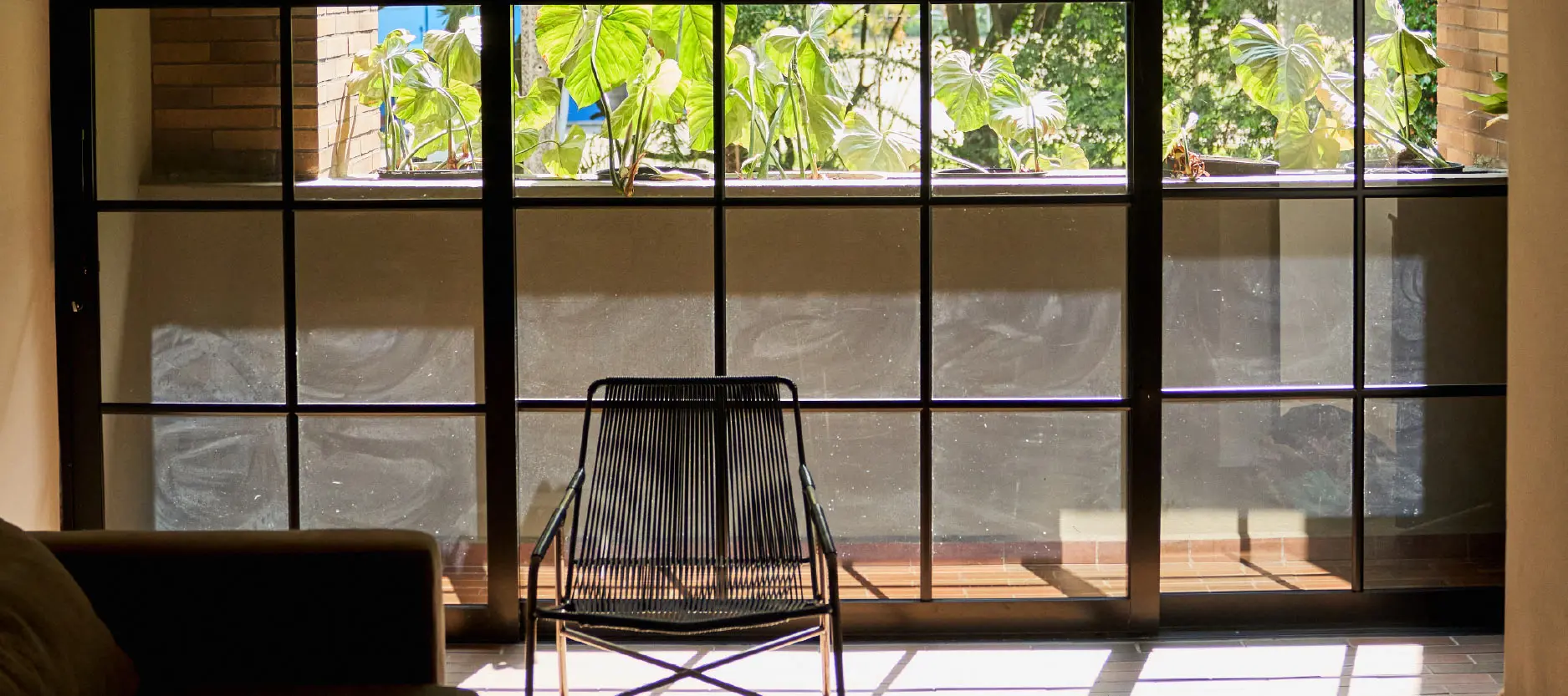 Silla frente a ventanal, plantas afuera, luz solar entrando a la habitaci&oacute;n.