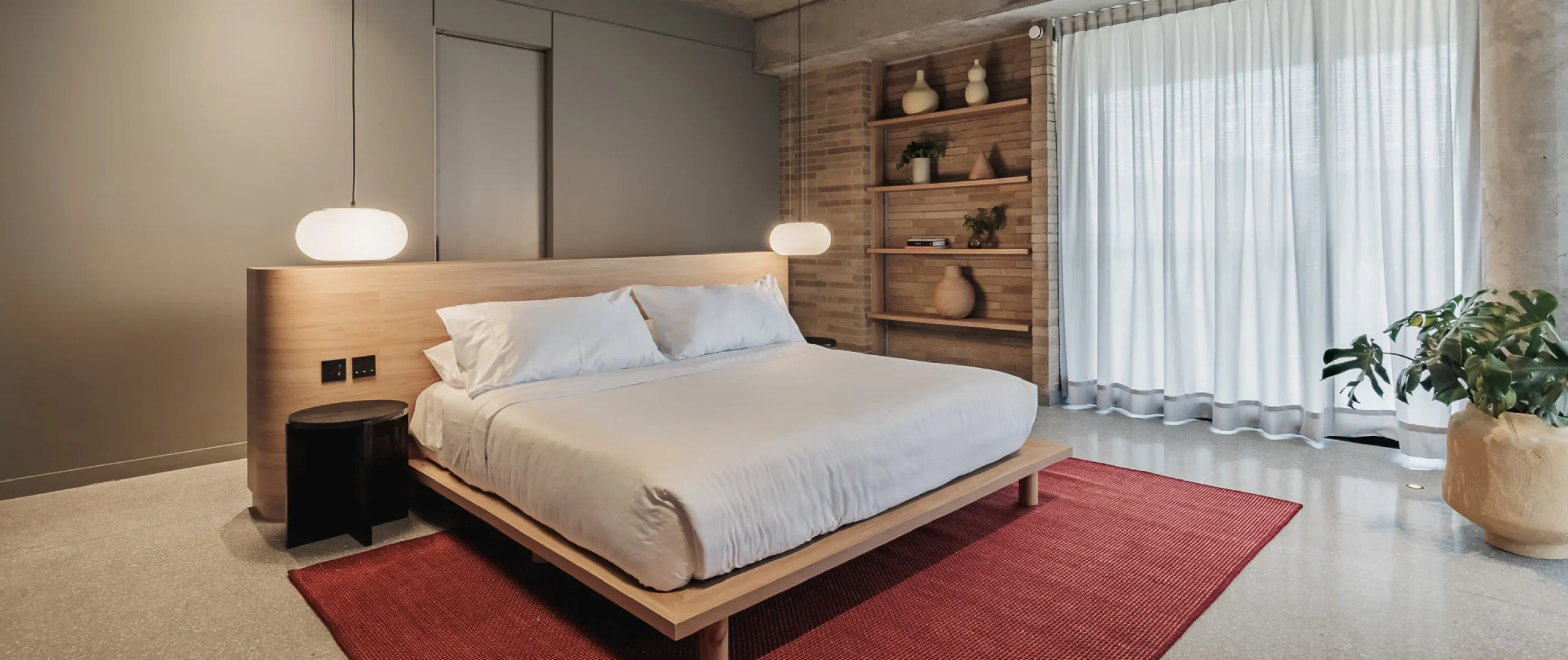 Dormitorio minimalista con cama, l&aacute;mparas y estanter&iacute;a de madera.