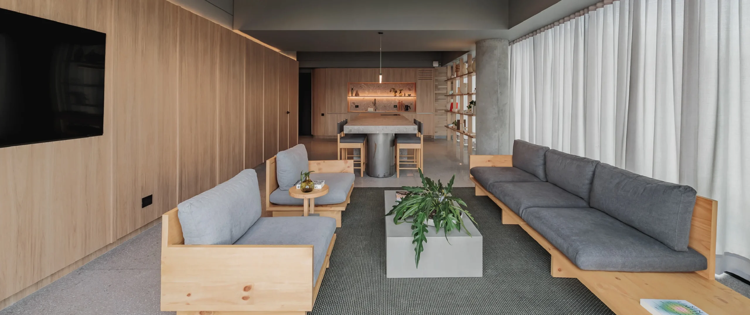 Sala moderna con sof&aacute;s grises, planta central y cocina al fondo.