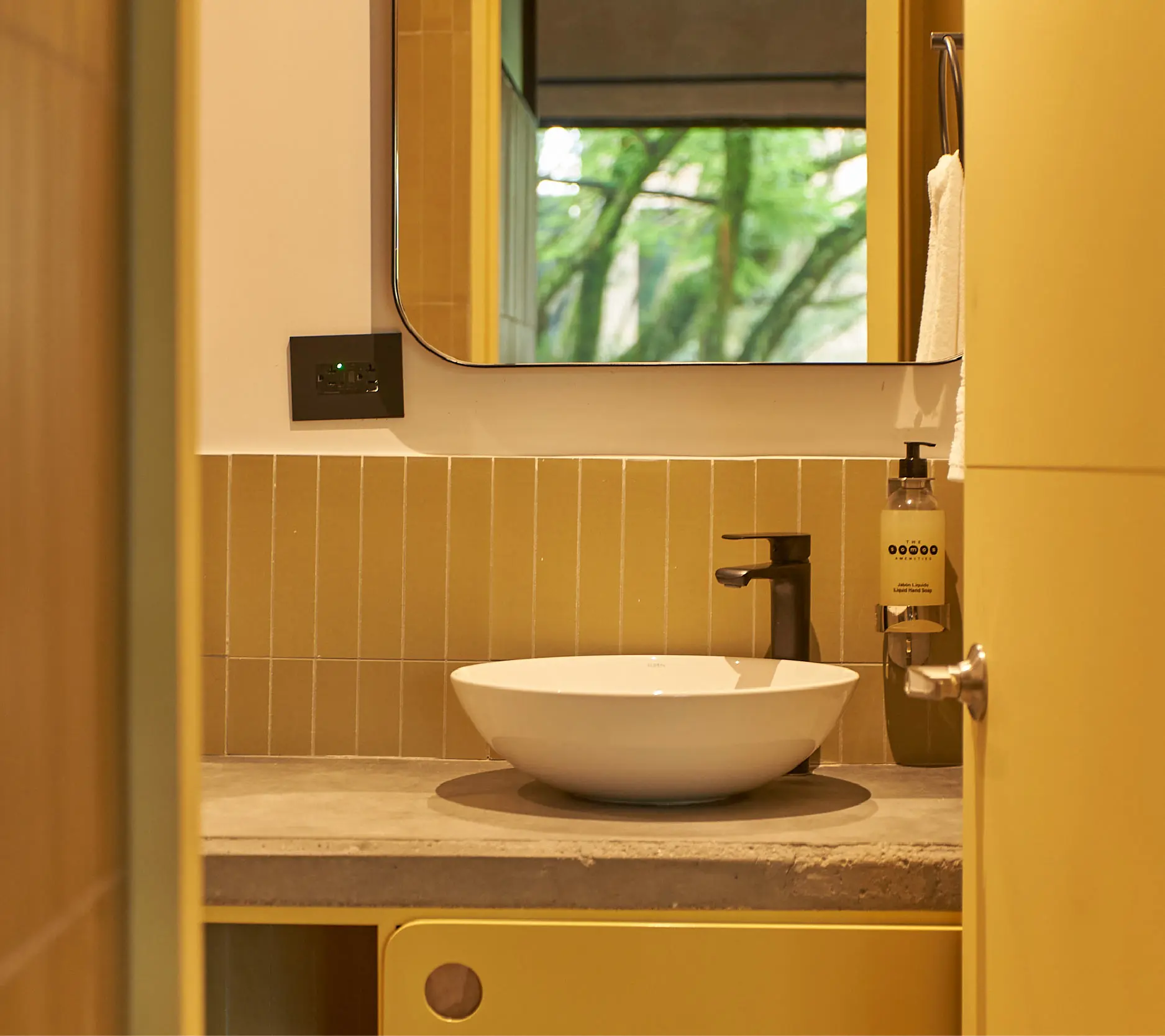 Ba&ntilde;o con lavabo blanco y paredes amarillas, espejo y ventana.