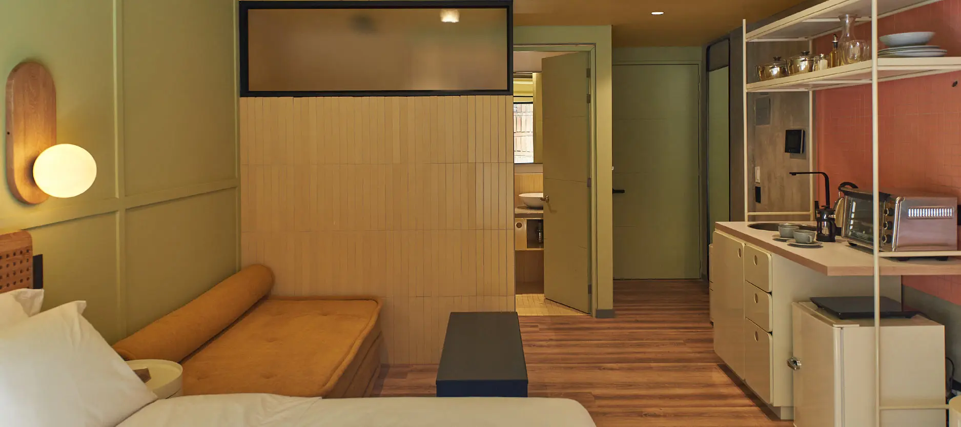 Habitaci&oacute;n moderna con cama y cocina integrada en tonos c&aacute;lidos.