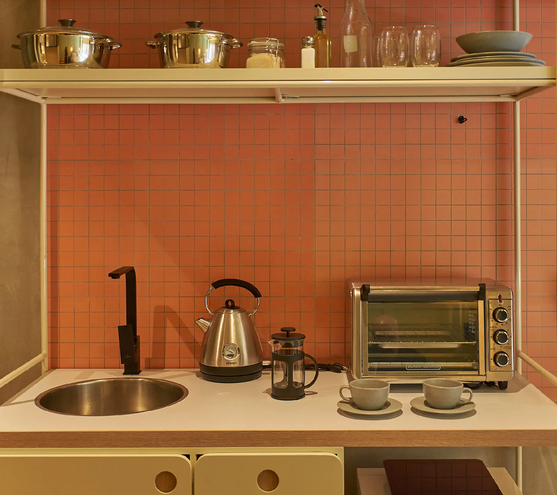 Cocina con azulejos naranjas, hervidor, cafetera y tostadora en la encimera.