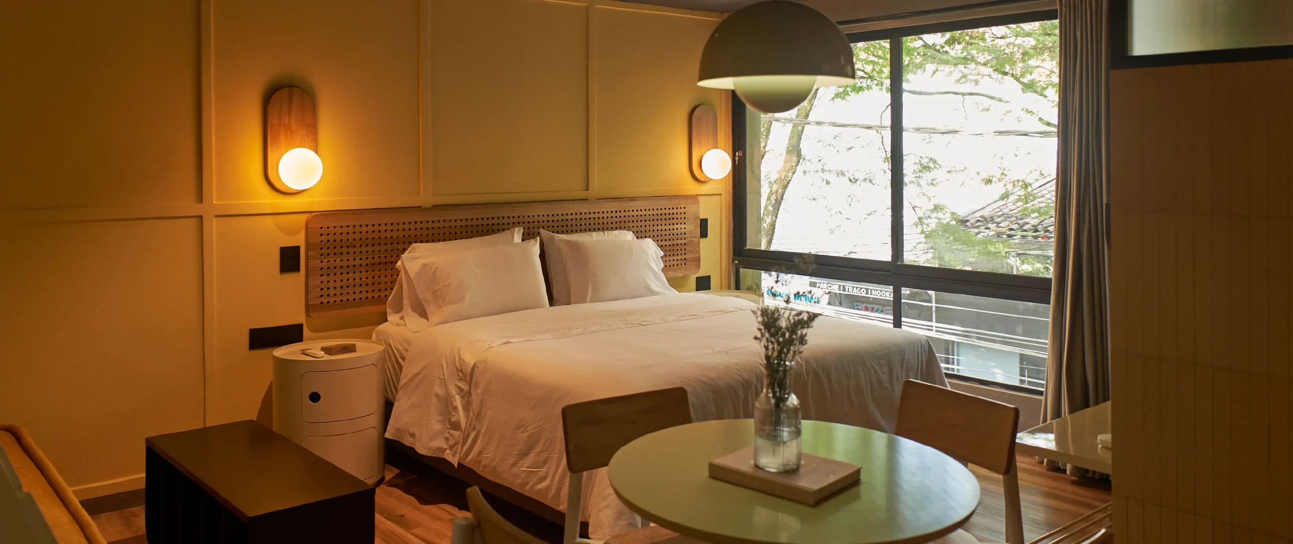 Habitaci&oacute;n moderna con cama, mesa y ventana grande con vista exterior.