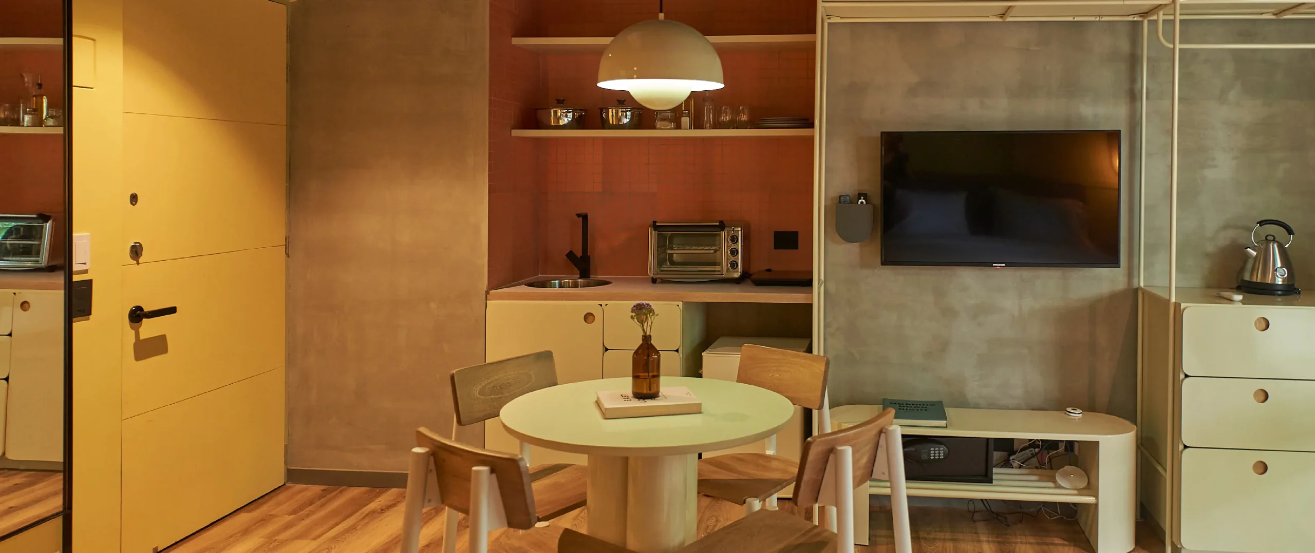 Cocina compacta con mesa, sillas, TV, horno y hervidor. Decoraci&oacute;n minimalista.