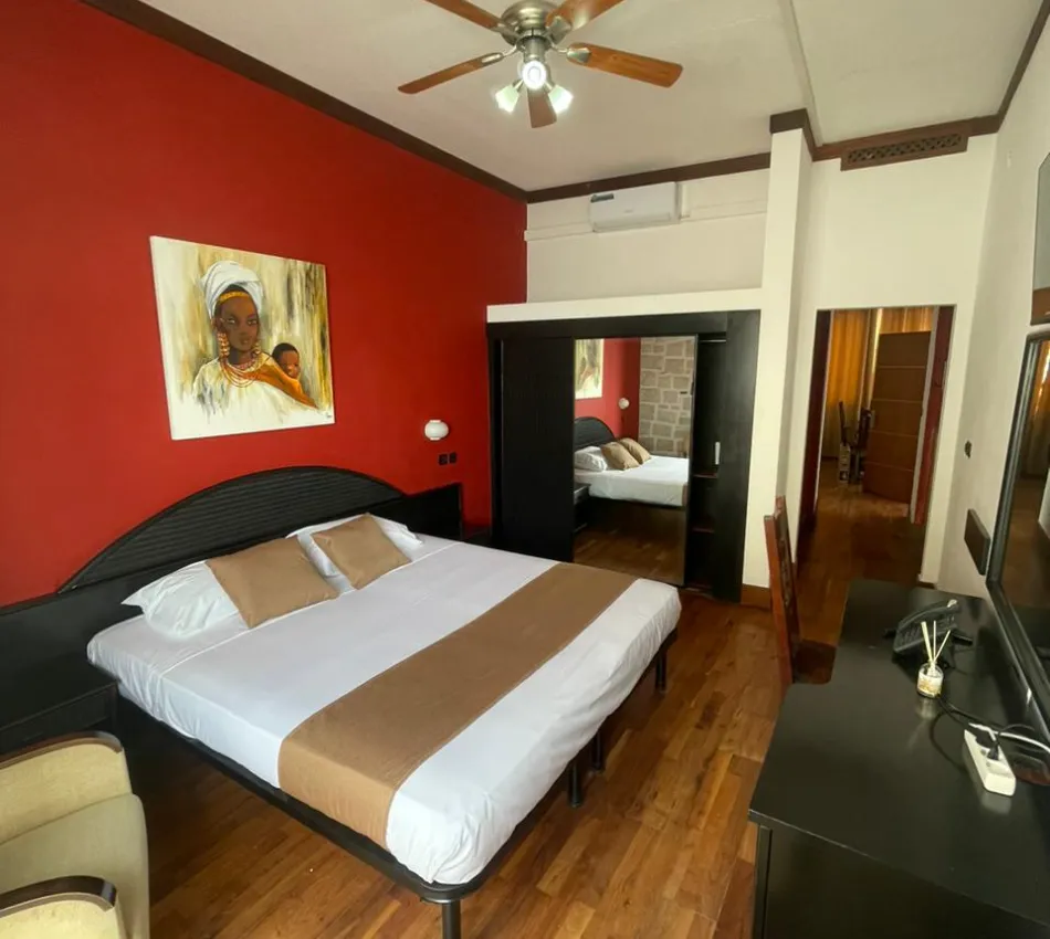 Quarto com cama de casal, parede vermelha e pintura acima da cabeceira.