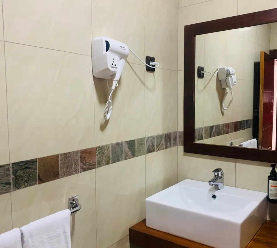 Banheiro com espelho, pia branca, secador de parede e toalha pendurada ao lado.