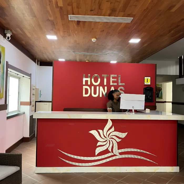 Recep&ccedil;&atilde;o do Hotel Dumas com balc&atilde;o vermelho e atendente ao computador.