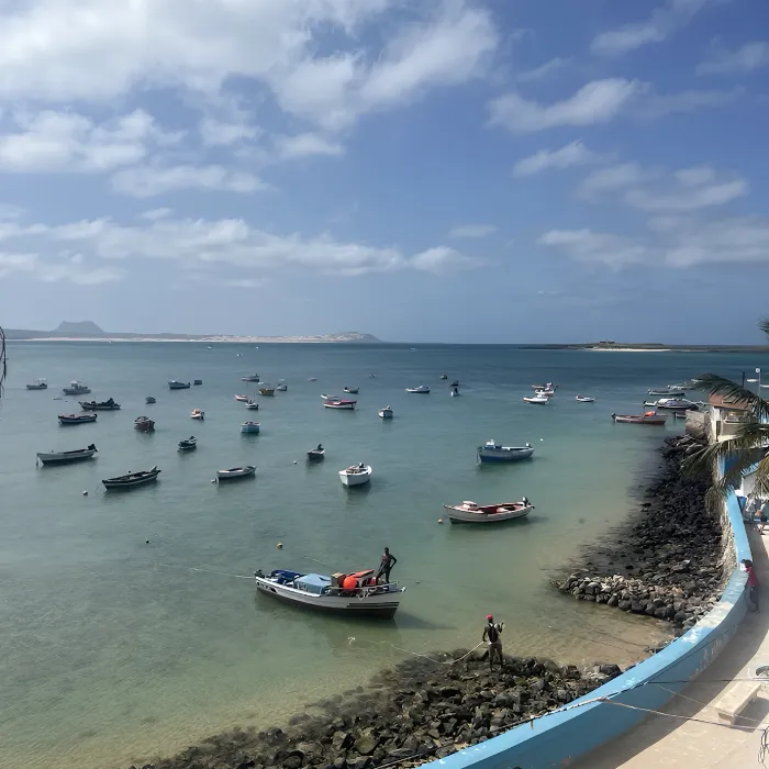 Barcos ancorados em uma ba&iacute;a tranquila, com c&eacute;u azul e algumas nuvens.