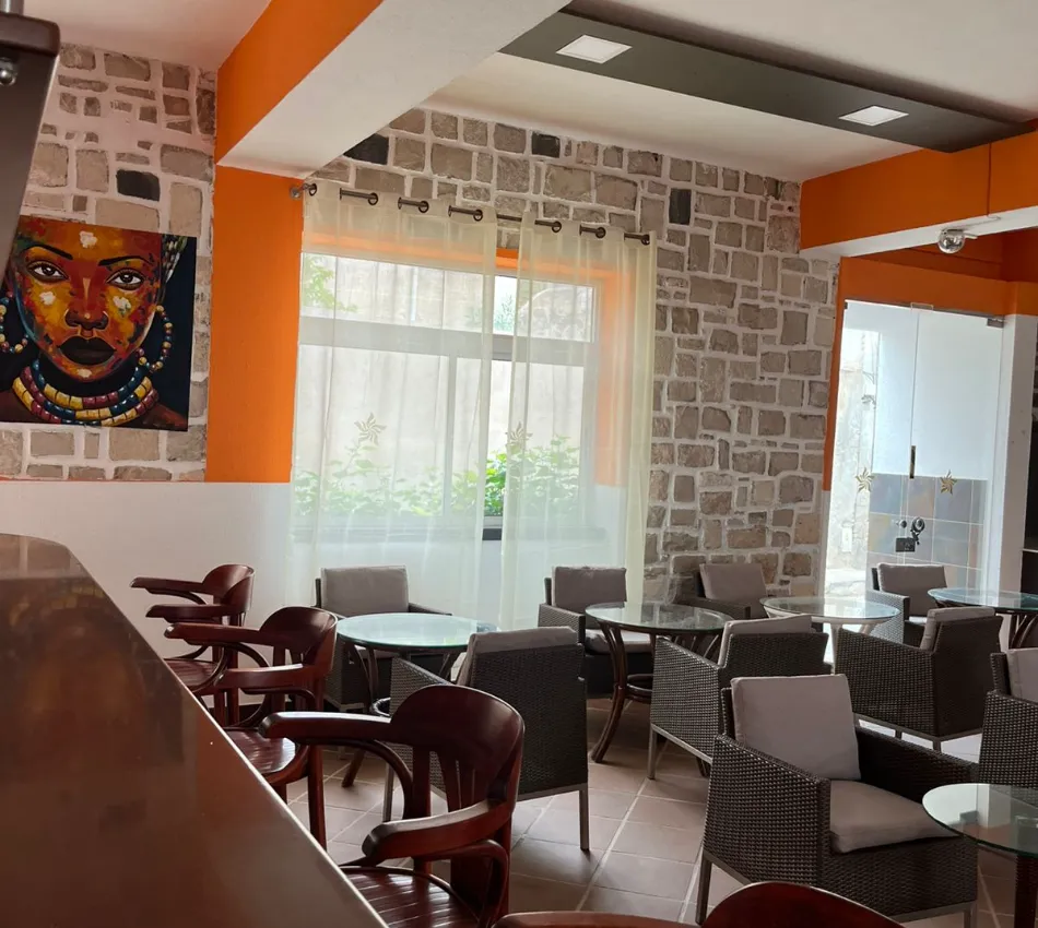 Sala com paredes de pedra, cadeiras de madeira e quadro colorido de rosto.