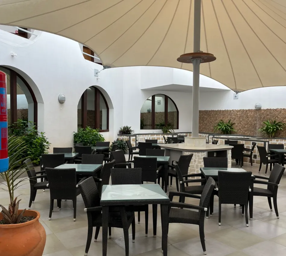 Espa&ccedil;o externo elegante com mesas e cadeiras sob cobertura, decorado com plantas verdes.