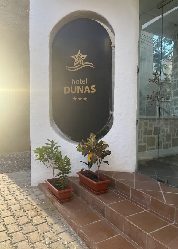 Entrada do hotel Dunas com tr&ecirc;s estrelas e plantas em vasos sobre degraus.