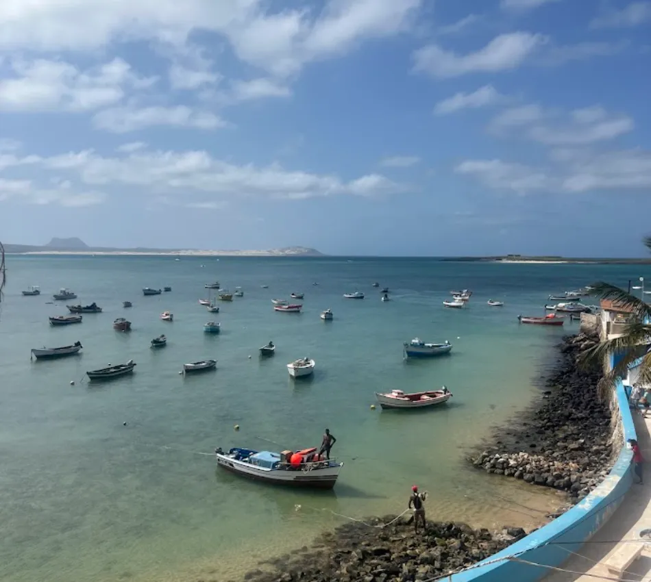 V&aacute;rios barcos ancorados em um mar azul sob c&eacute;u parcialmente nublado, vista do cais.