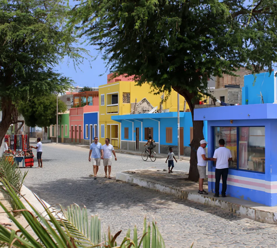 Rua com casas coloridas, &aacute;rvores e pessoas caminhando e andando de bicicleta.