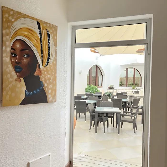 Pintura de mulher com turbante ao lado de porta que d&aacute; acesso a &aacute;rea externa com mesas e cadeiras.