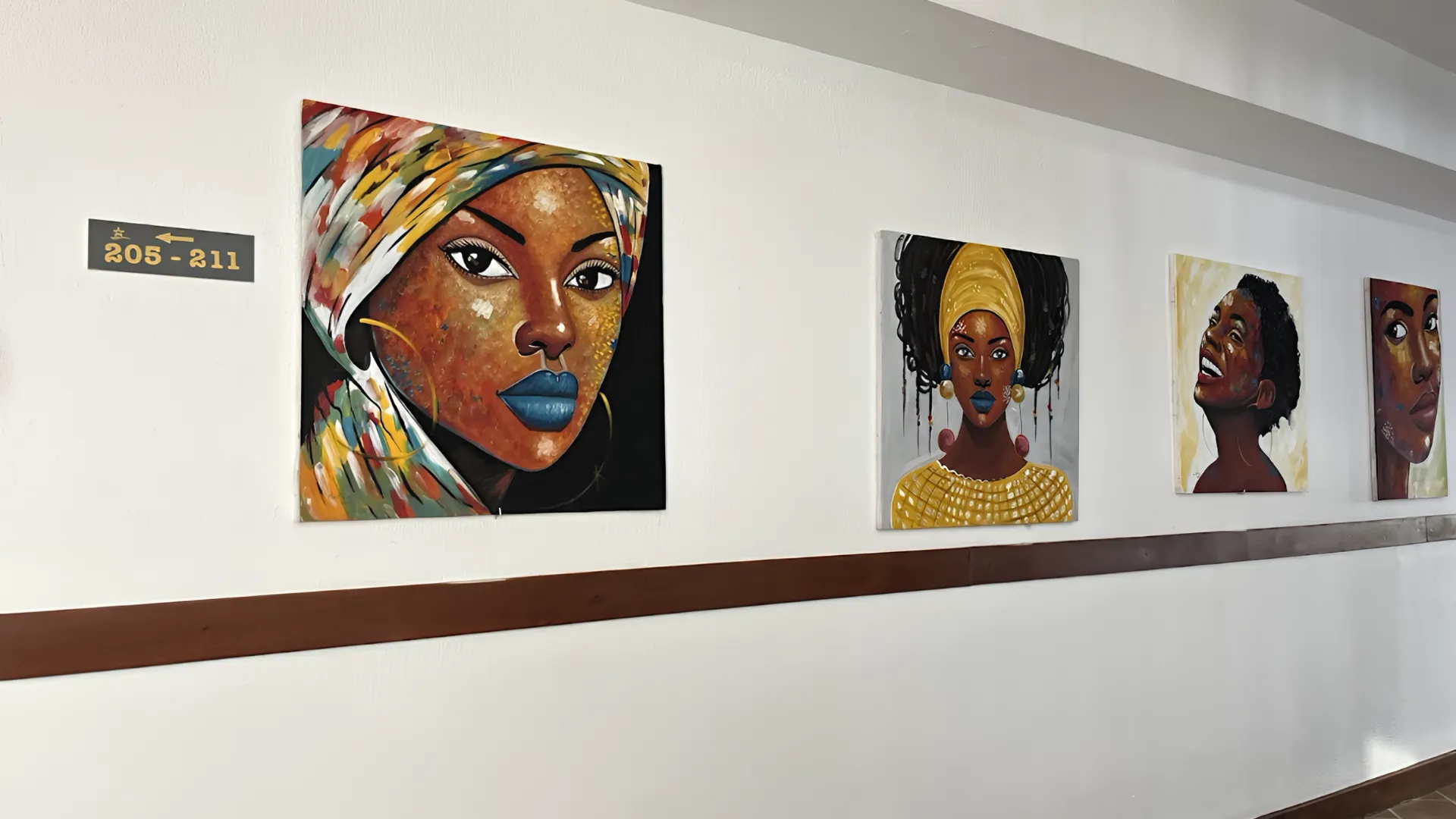 Pinturas coloridas de rostos em uma parede branca de corredor, com sinal de numera&ccedil;&atilde;o de portas.