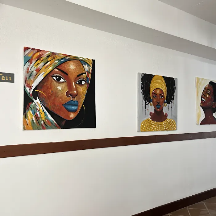 Tr&ecirc;s pinturas coloridas de mulheres africanas em uma parede branca.