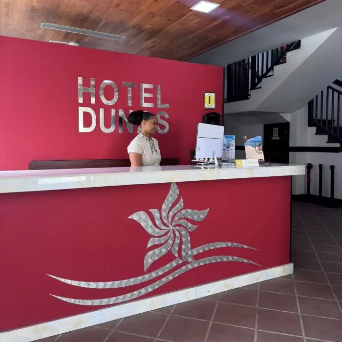 Recep&ccedil;&atilde;o do Hotel Dumas com balc&atilde;o vermelho e atendente ao computador.