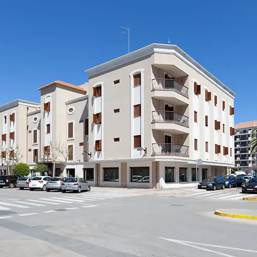 Edificio de esquina con balcones y coches estacionados en la calle.