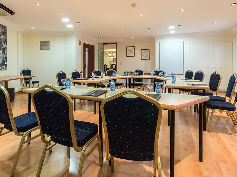 Sala de reuniones con mesas en U y sillas azules, lista para conferencias.
