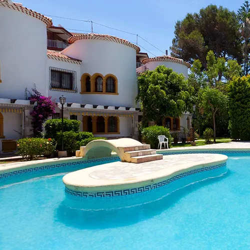 Casa con piscina y puente en un entorno verde y soleado.