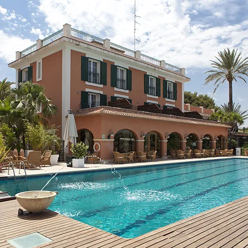Edificio junto a piscina con palmeras y cielo azul.