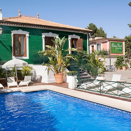 Piscina azul junto a edificio verde con vegetaci&oacute;n y mobiliario blanco.