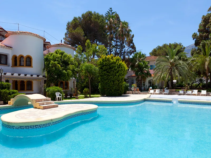 Piscina grande rodeada de &aacute;rboles y un edificio blanco con ventanas arqueadas.