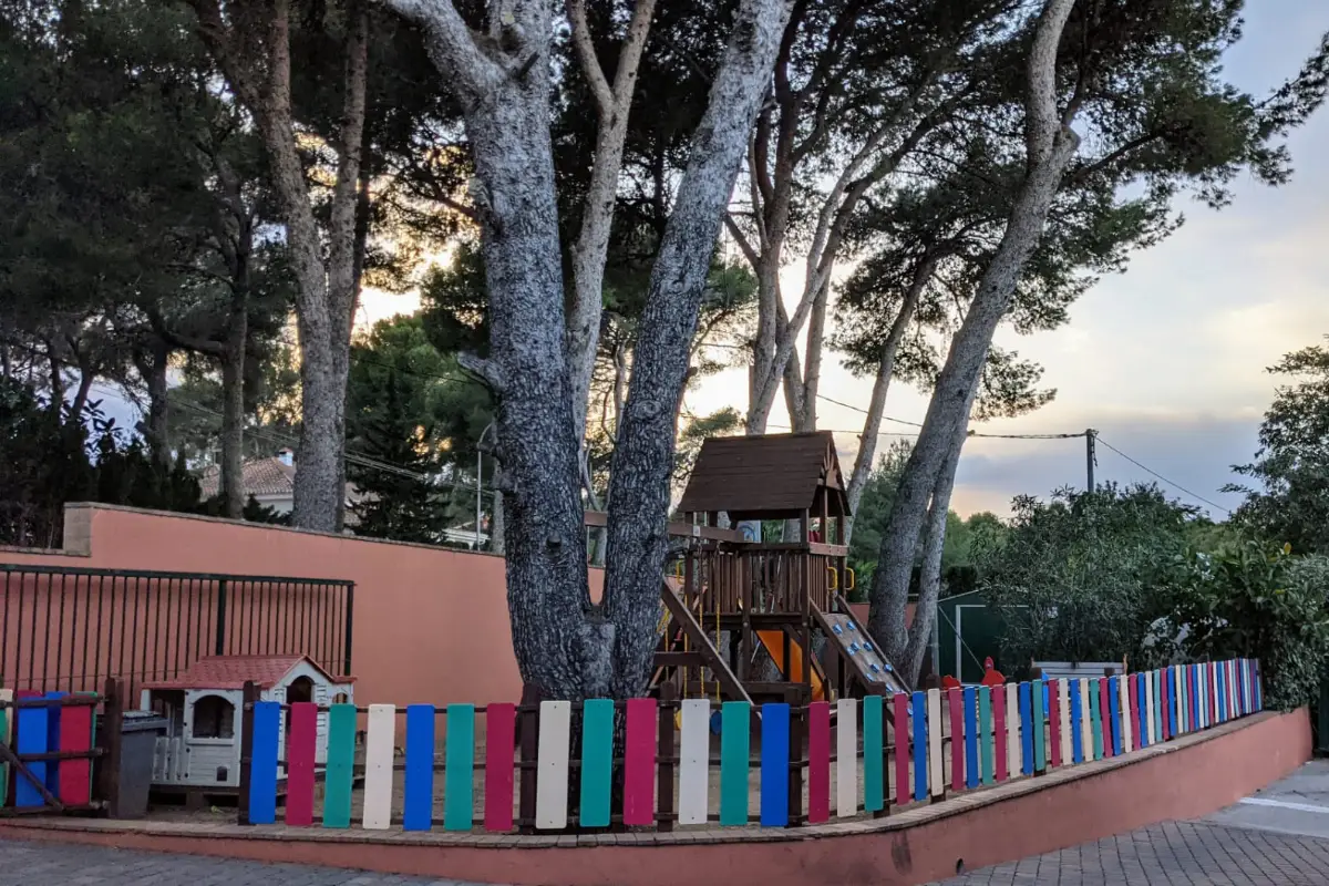 Parque infantil con vallas de colores y &aacute;rboles al atardecer