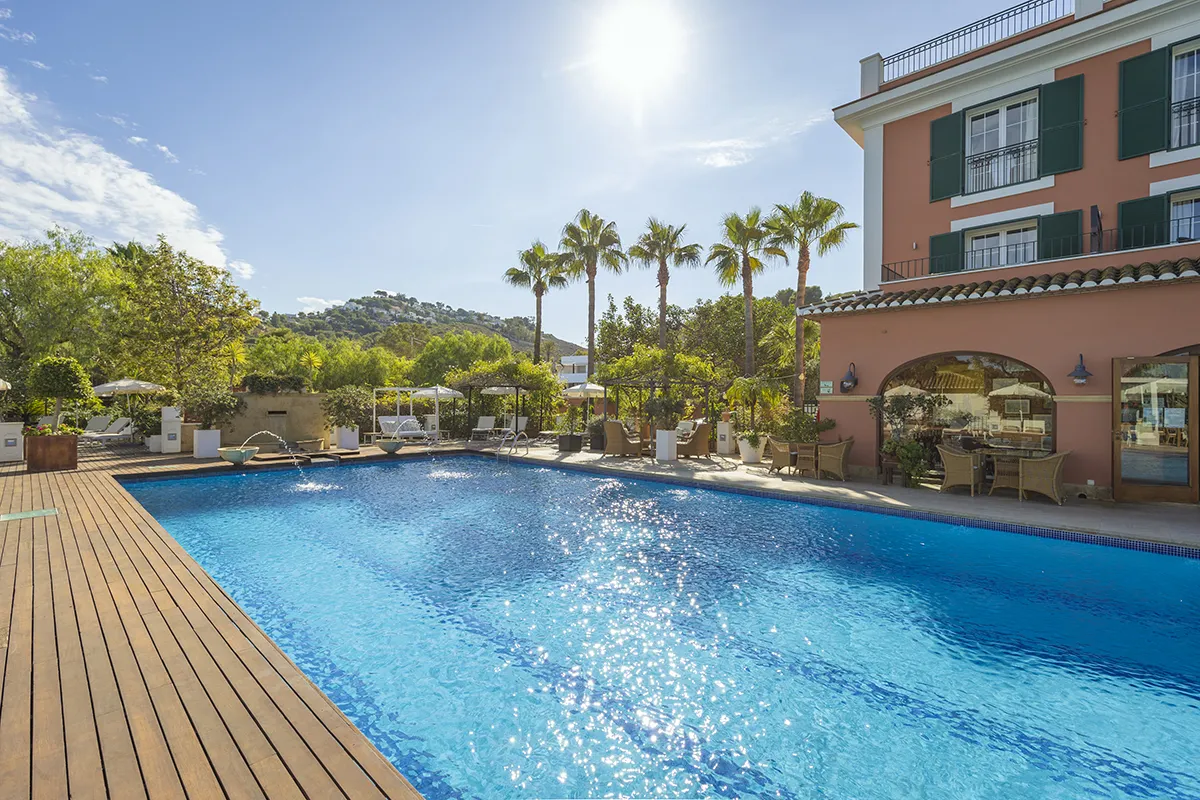 Piscina reluciente junto a un edificio con palmeras y colinas al fondo.
