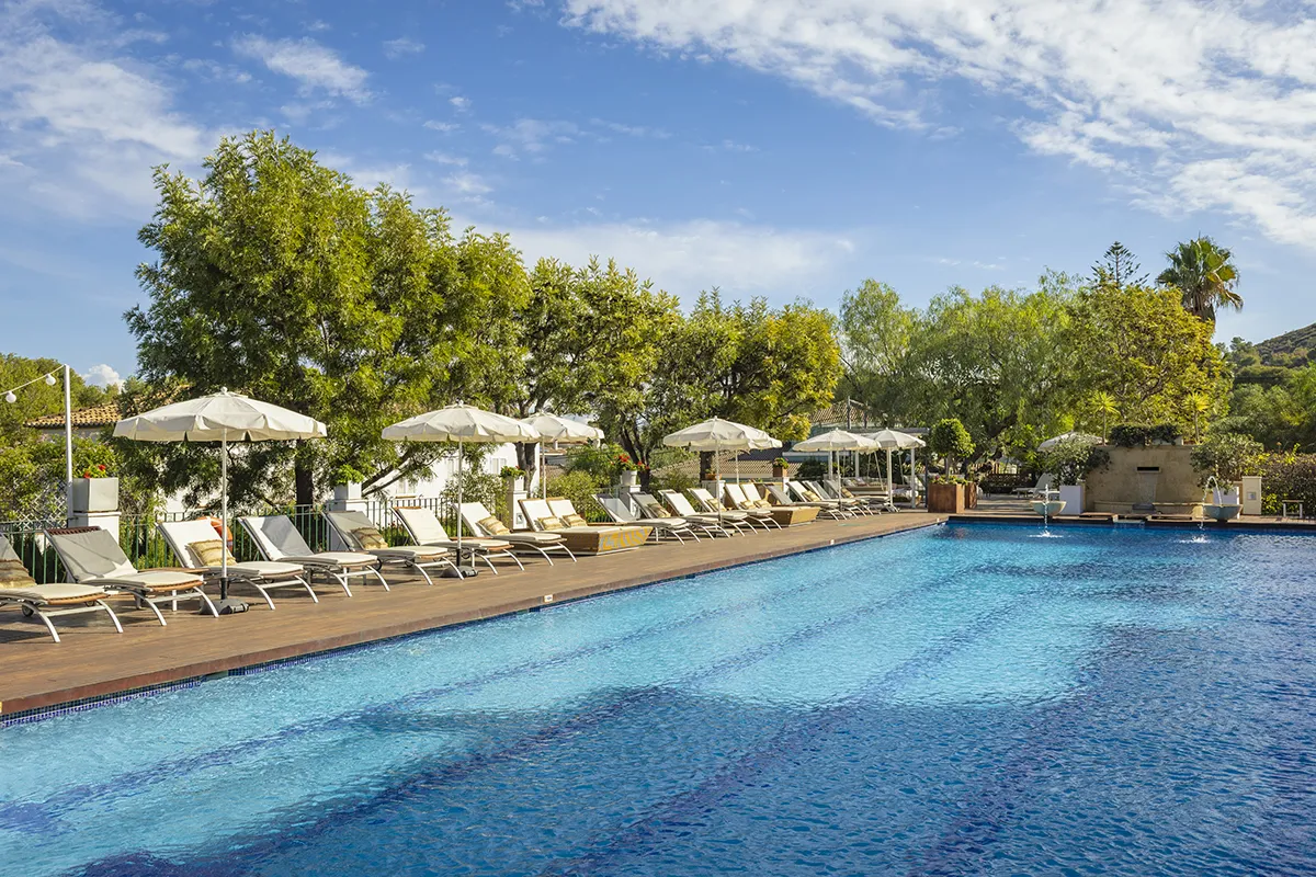 Piscina al aire libre con sombrillas y tumbonas bajo un cielo azul.